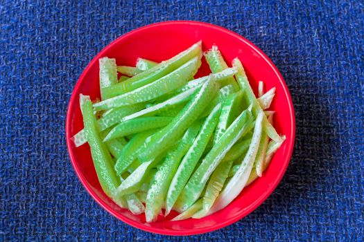 Green strips of cucumbers on scarlet plate on dark blue textile background