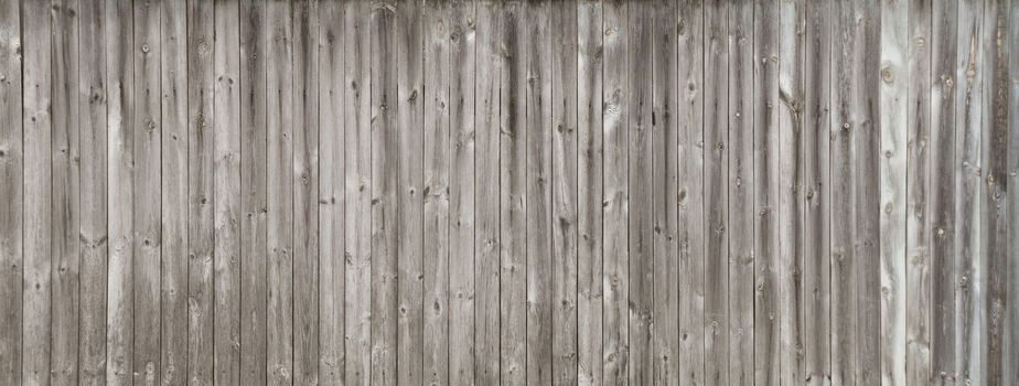 Long gray wooden fence consisting of old weathered unpainted boards
