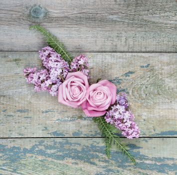 Decorative composition consisting of pink roses, violet lilac flowers and green leaves on the old wooden background. Flat lay, top view