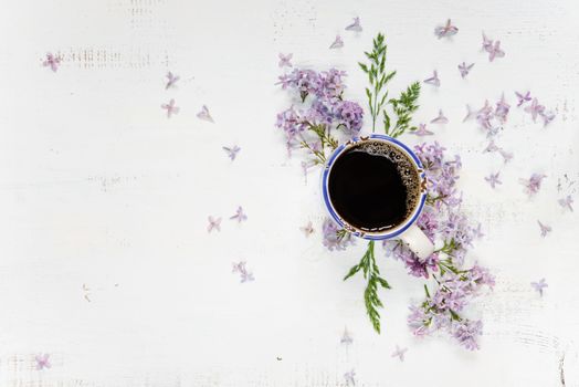 Cup of coffee and purple lilac flowers on the wooden background; flat lay, top view
