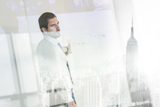 Business man making a presentation in front of whiteboard. Business executive delivering a presentation to his colleagues during meeting or in-house business training. View through glass.