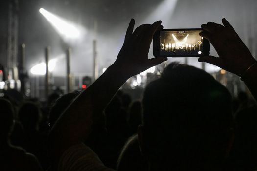 Silhouette of hands recording videos at music concert. Pop music concert with lights, smoke and lots of people