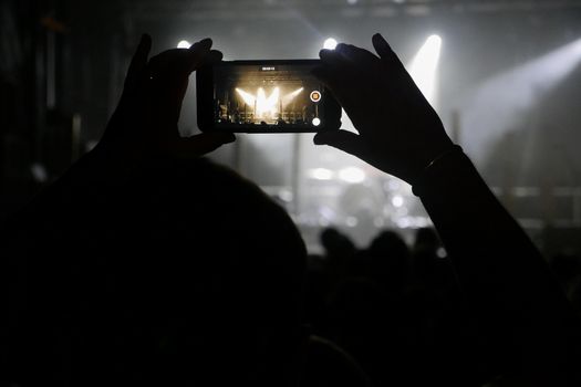 Silhouette of hands recording videos at music concert. Pop music concert with lights, smoke and lots of people