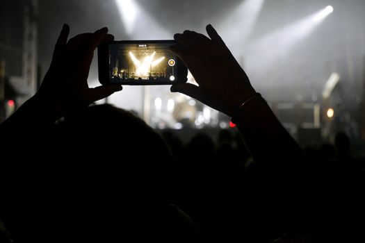 Silhouette of hands recording videos at music concert. Pop music concert with lights, smoke and lots of people
