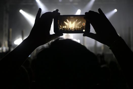 Silhouette of hands recording videos at music concert. Pop music concert with lights, smoke and lots of people