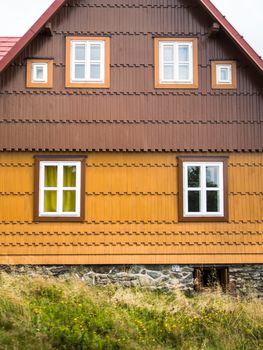 Authentic rustic yellow and brown mountain cottage front with windows and stones in Bohemian Forrest, Czech republic, Europe