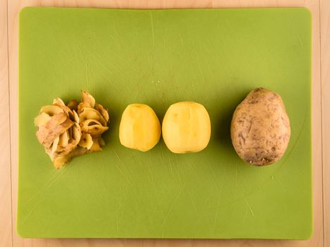 Two unpeeled and one peeled potatoes with skinsin center of green plastic board, simple food preparation illustration, vegetarian dieting, top view still life with bottom copyspace