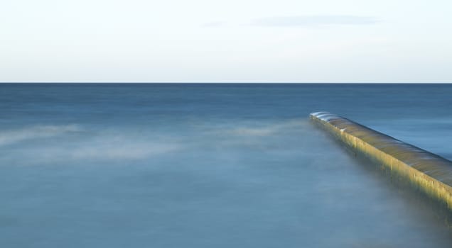 Calm Ocean with Breakwater Structure with clouds in the sky.
