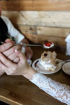 the groom holds the spoon meringue with strawberries on the background of the table with coffee