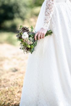 the bride's bouquet from cones and cotton close up in the hands of the bride lace dress forest backdrop