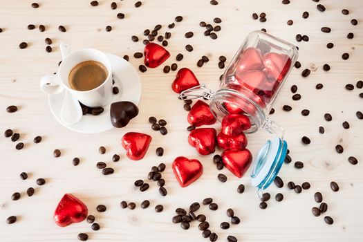 Red chocolate hearts in a glass jar and a cup of espresso coffee with coffee beans on a table viewed from above