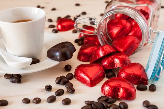 Red chocolate hearts in a glass jar and an espresso coffee with coffee beans on a table