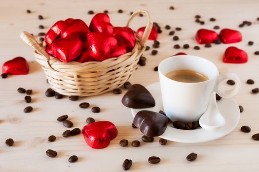 Red chocolate hearts in a small basket and an espresso coffee with coffee beans on a table