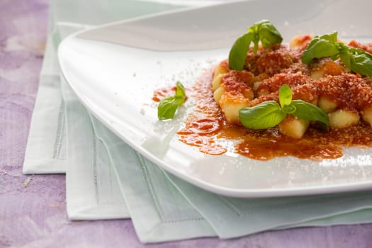 Gnocchi pasta with tomato sauce basil and parmesan cheese in a square white plate over a napkin