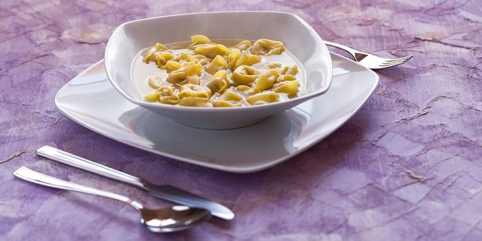 Tortellini in broth in a white square plate with cutlery