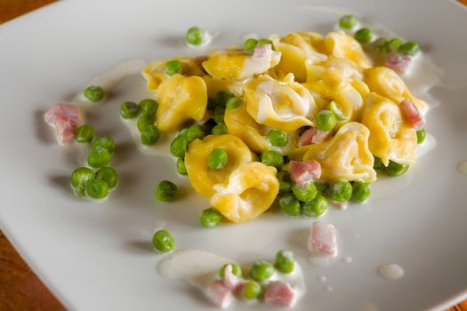 Tortellini with cream ham and peas on a white square plate
