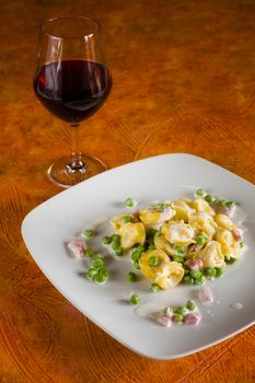 Tortellini with cream ham peas and red wine on a white square plate