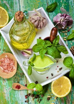 Ripe Raw Ingredients and Freshly Made Creamy Pesto Sauce in Glass Gravy Boat in White Wooden Tray. Top View on Cracked Wooden background