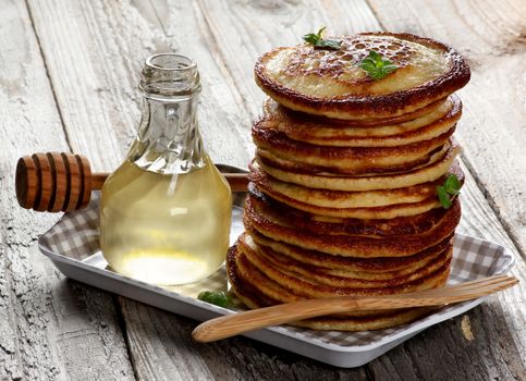 Stack of Delicious Homemade  Pancakes with Mint Leafs, Honey in Glass Container and Honey Dipper in Checkered Tray closeup on Wooden background
