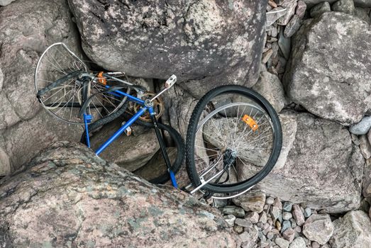 Broken bicycle lying on the rocky bottom of a dried-up riverbed.