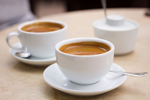 Coffee break in cafe, two cups of coffee and sugar bowl on marble table top