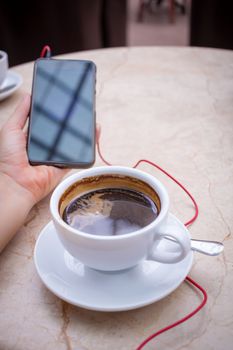 Smartphone at hand and americano coffee in white cup at marble table top