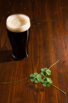Pint of black beer and three shamrocks on a wood background.