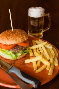 Hamburger with salad and tomatoes matched by fried potatoes and beer on a table
