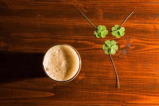 Pint of black beer and three shamrocks on a wood background seen from above.