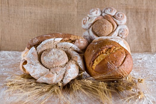 Assortment of baked bread with wheat on board and jute background