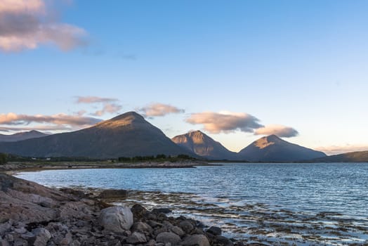 Summer landscape with rocky shore and sharp mountain peaks in Norway.