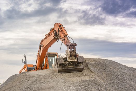 Frontal view of an orange excavator climbed on top of a ballast pile.