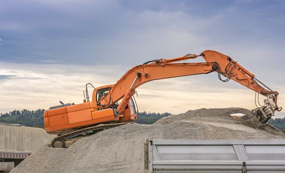 Orange excavator, climbed on a ballast pile, loading material in a trailer.