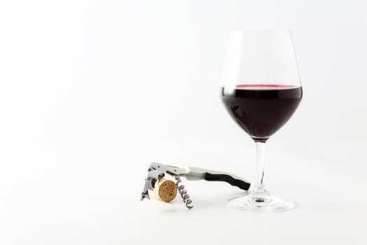 Glass of red wine with cork and corkscrew on a white background