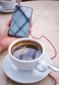 Smartphone at hand and americano coffee in white cup at marble table top