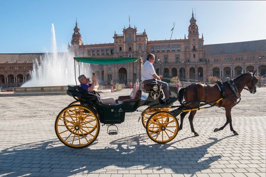 Seville, Spain - August 28, 2015: Horse carriage with tourists at Plaza de Espana in Seville. It is a landmark example of the Renaissance Revival style in Spanish architecture.