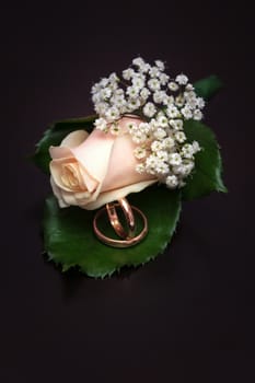 Wedding rings and pibk boutonniere lie on the brown background