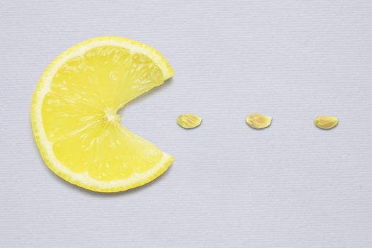 Creative concept photo of a lemon slice eating seeds on grey background.