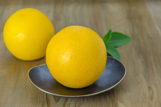 ripe orange with leaves on dish over wooden background