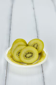 golden kiwi fruit and sliced on dish over white wooden background
