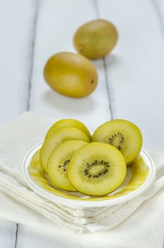 golden kiwi fruit and sliced on dish over white wooden background