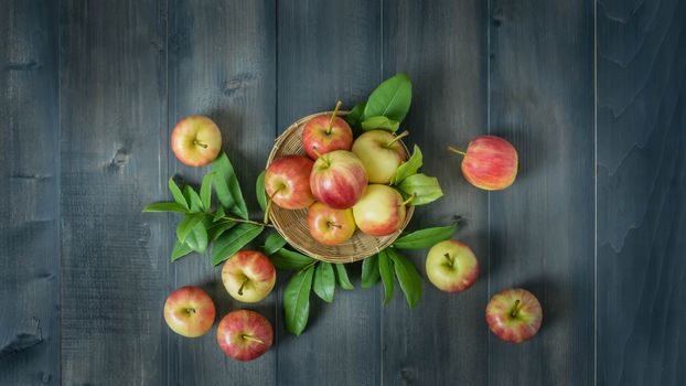 Top view red and yellow apple with leaves and  bamboo basket on wooden background with free space for text