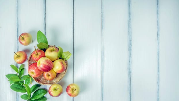 Top view red and yellow apple with leaves and  bamboo basket on  white wooden background with free space for text