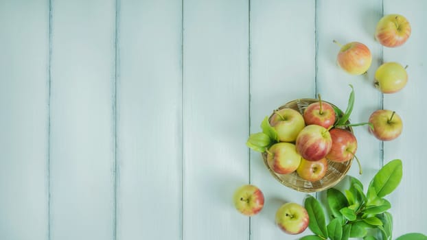 Top view red and yellow apple with leaves and  bamboo basket on  white wooden background with free space for text