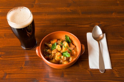 Traditional Irish Stew on a brown bowl with a pint of stout beer and a spoon over a napkin on a table.