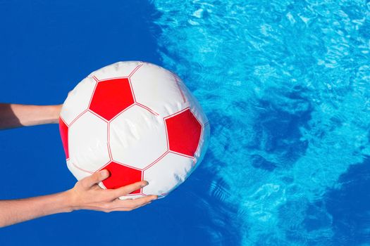 Hands of boy holding beach ball above swimming pool water invitation to play