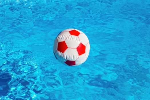 Red white beach ball floating on water in blue swimming pool