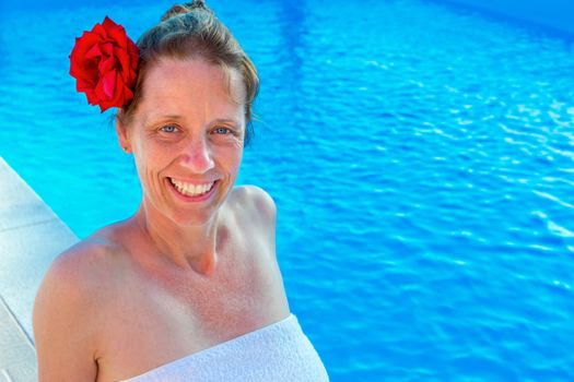 European middle aged woman with red rose in hair and towel at swimming bath