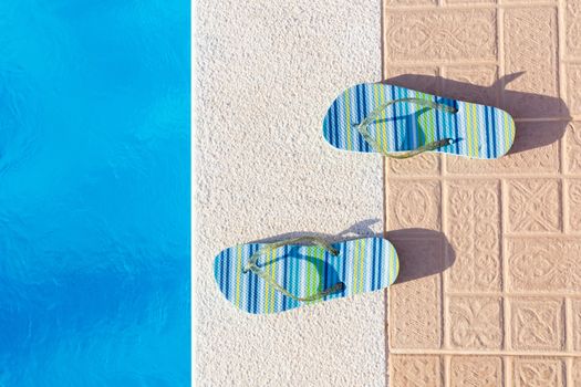 Pair of striped bathing slippers at edge of swimming pool