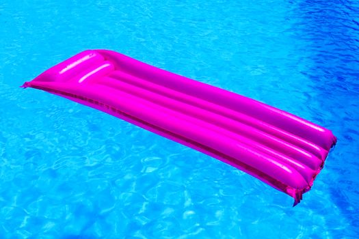 Pink air mattress floating on water of blue swimming pool